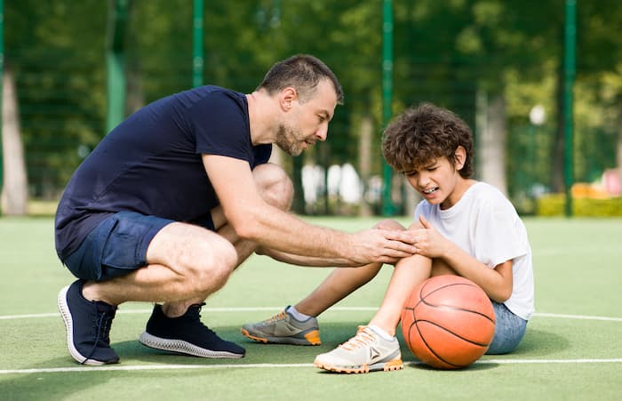 Padre che consola il figlio infortunato durante una partita di basket all’aperto